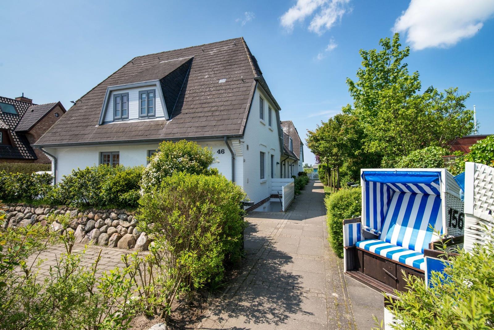 Weiße Ferienhaus mit Dachgaube und blau-weißem Strandkorb.