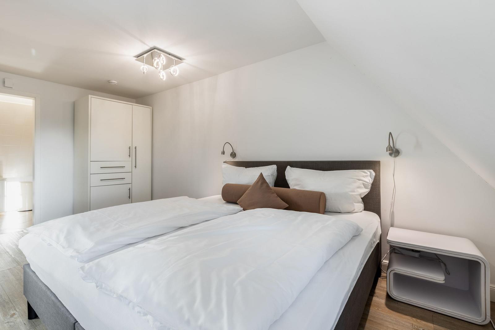 Schlafzimmer mit Doppelbett, weißen Wänden und moderner Beleuchtung.