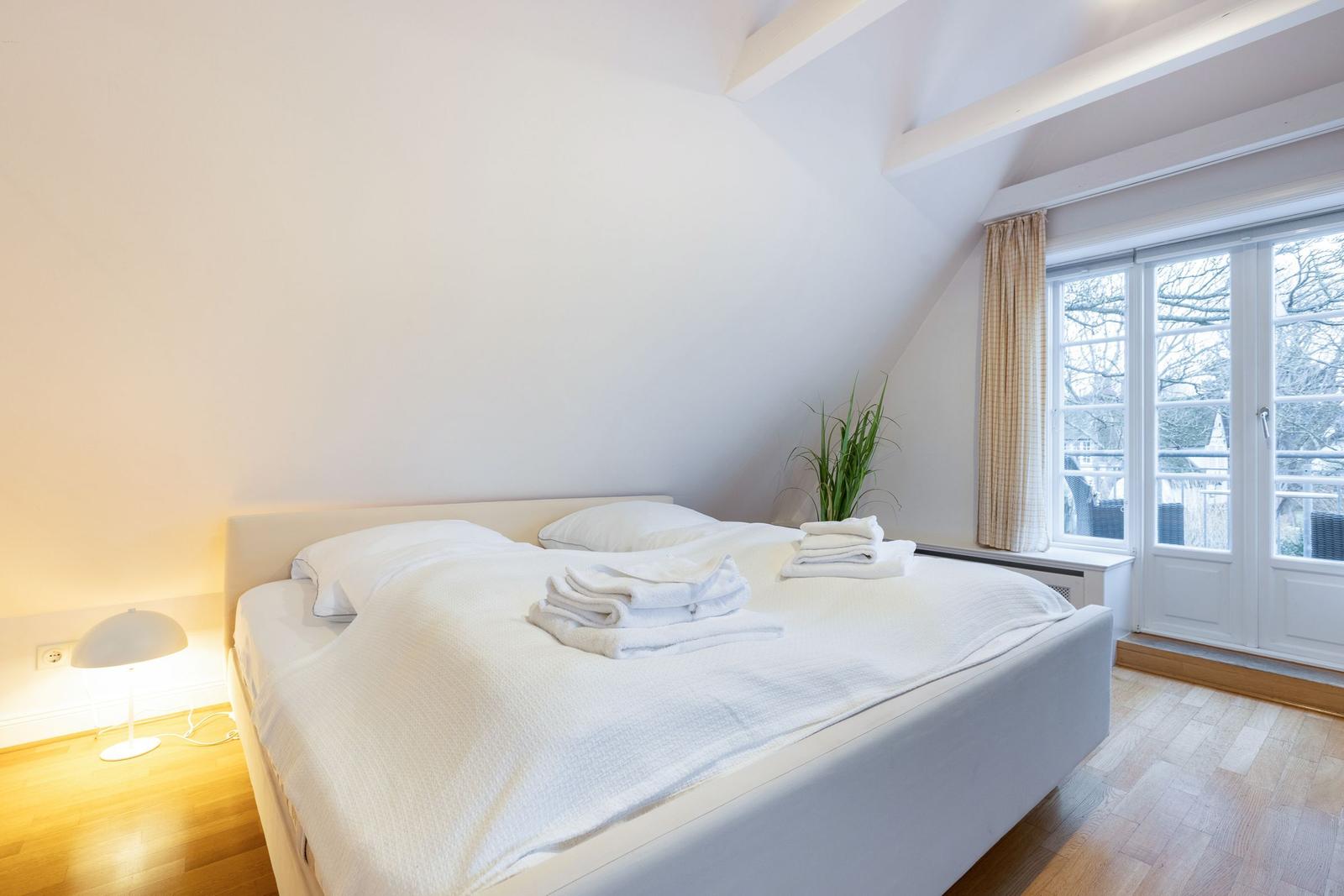 Schlafzimmer mit Doppelbett, Fenster und Holzboden.