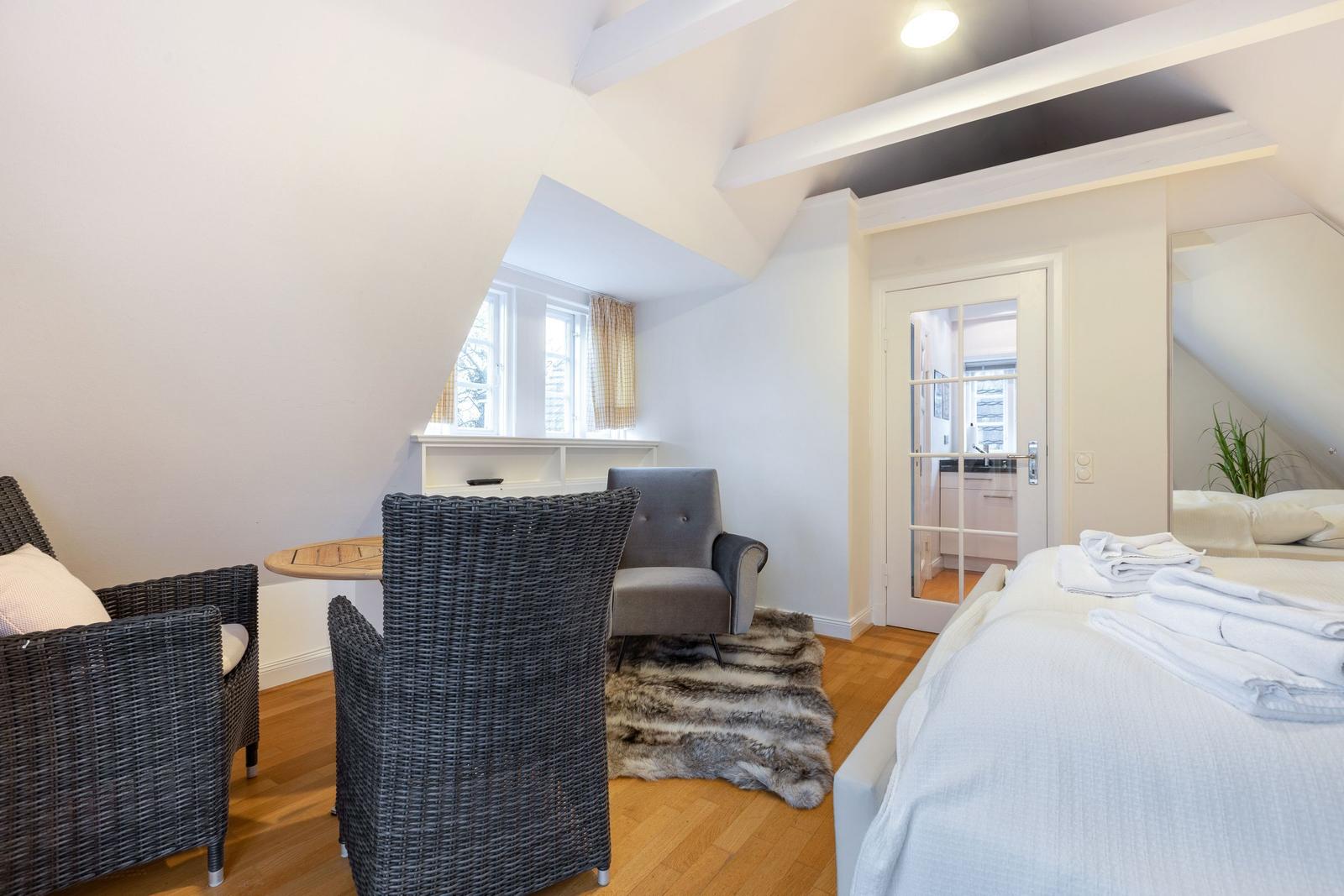 Schlafzimmer mit Bett, Stuhl, Tisch und Fenster. Holzboden und Deckenbalken.