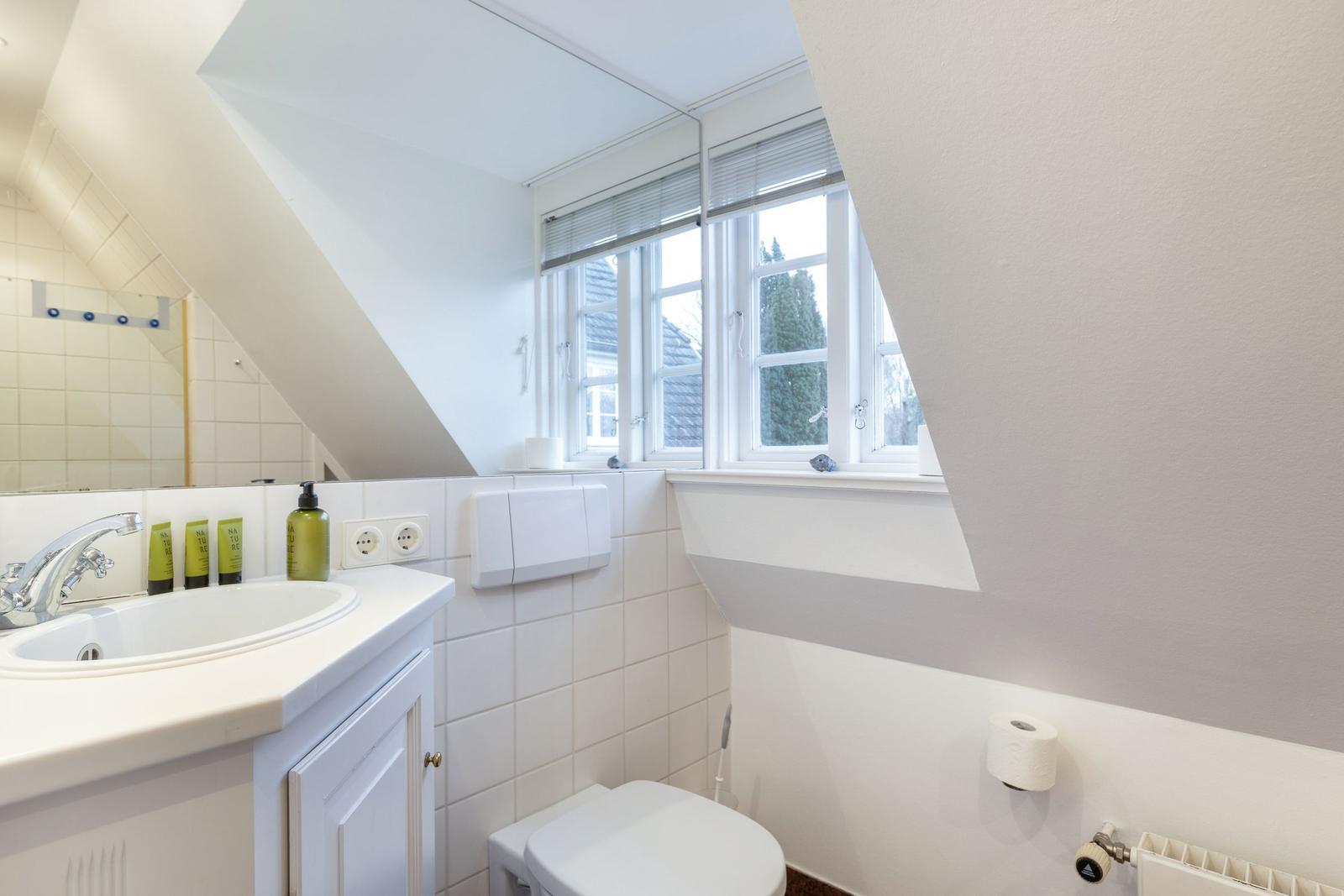Badezimmer mit Waschbecken, Toilette und Fenster mit Blick nach draußen.