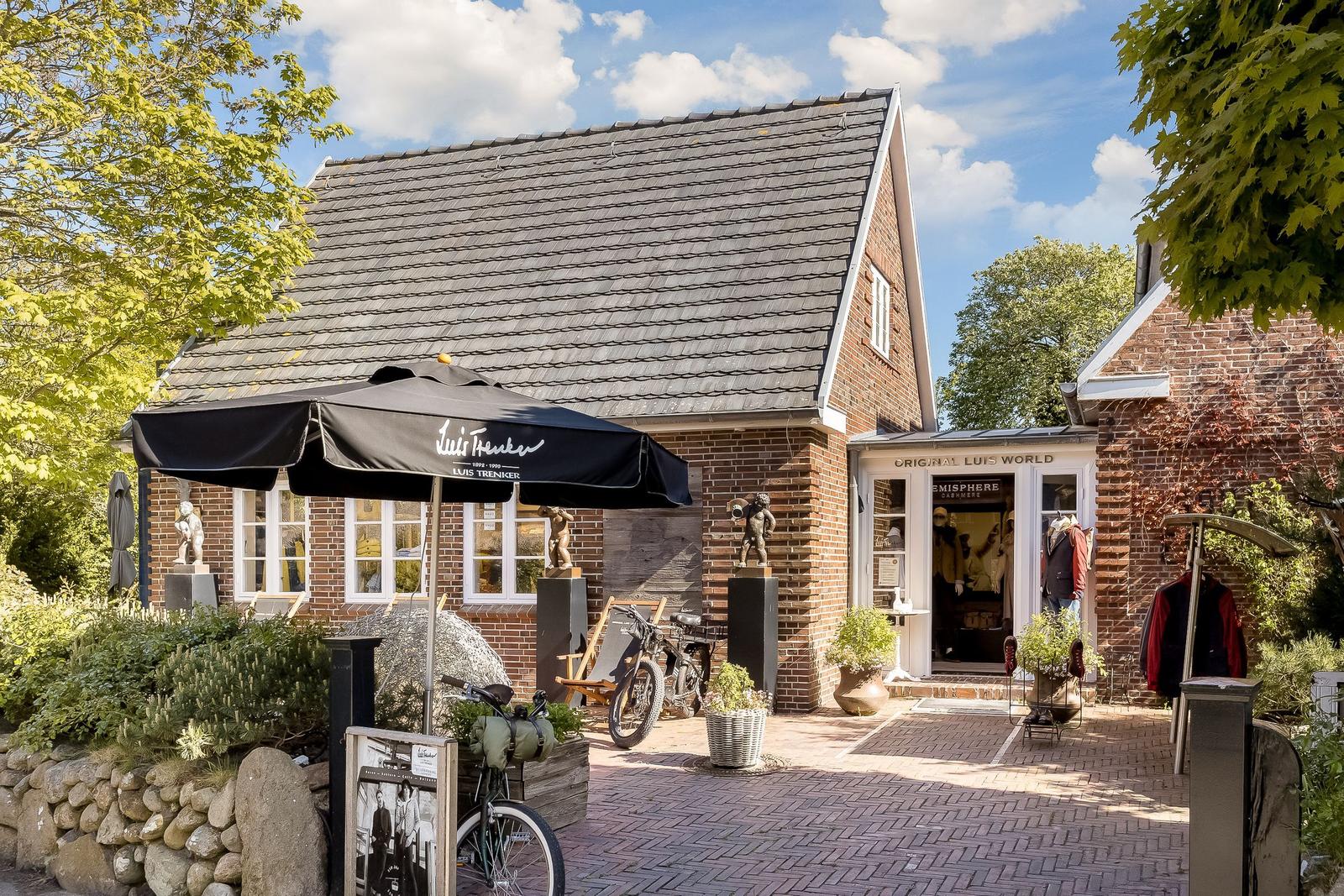 Ein Haus mit Schopf und Terrasse, auf der ein Sonnenschirm und Fahrräder stehen.