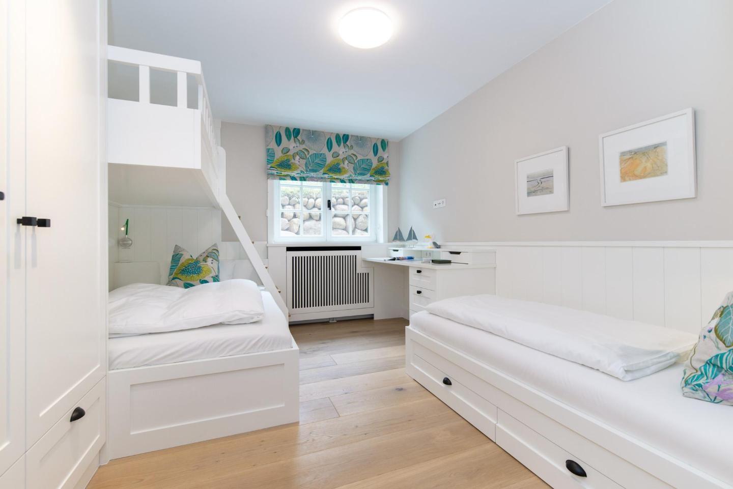 Room with loft bed, desk, and window with floral roller blind.