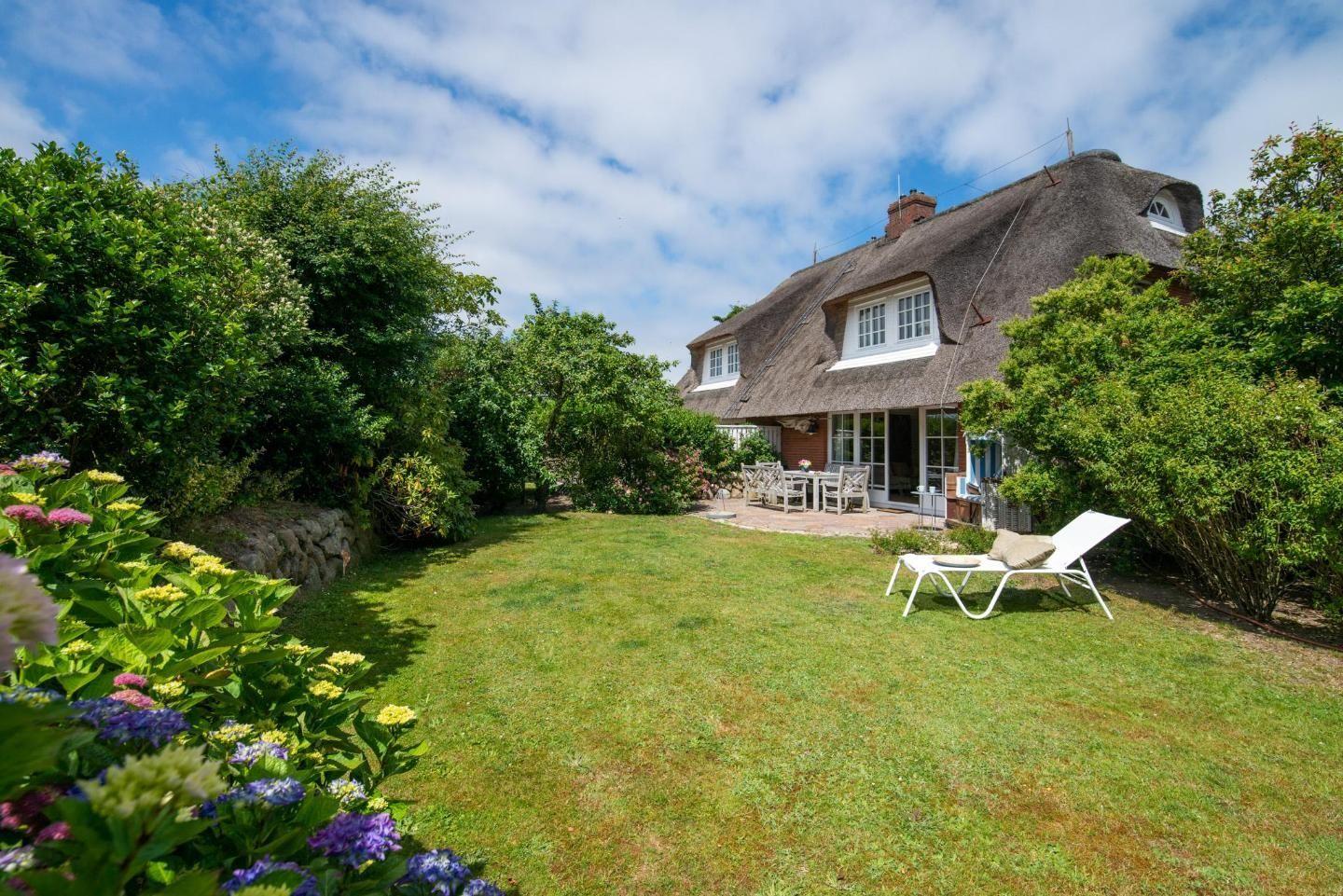 House with thatched roof, garden, lounge chair, and terrace with table and chairs.