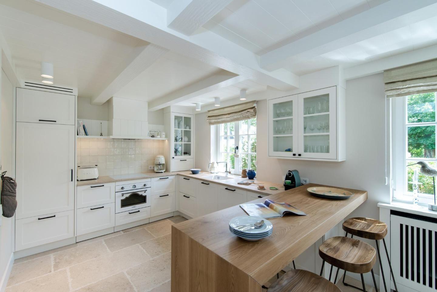 Kitchen with wooden island, white cabinets, and stone floor. Windows with view of greenery.