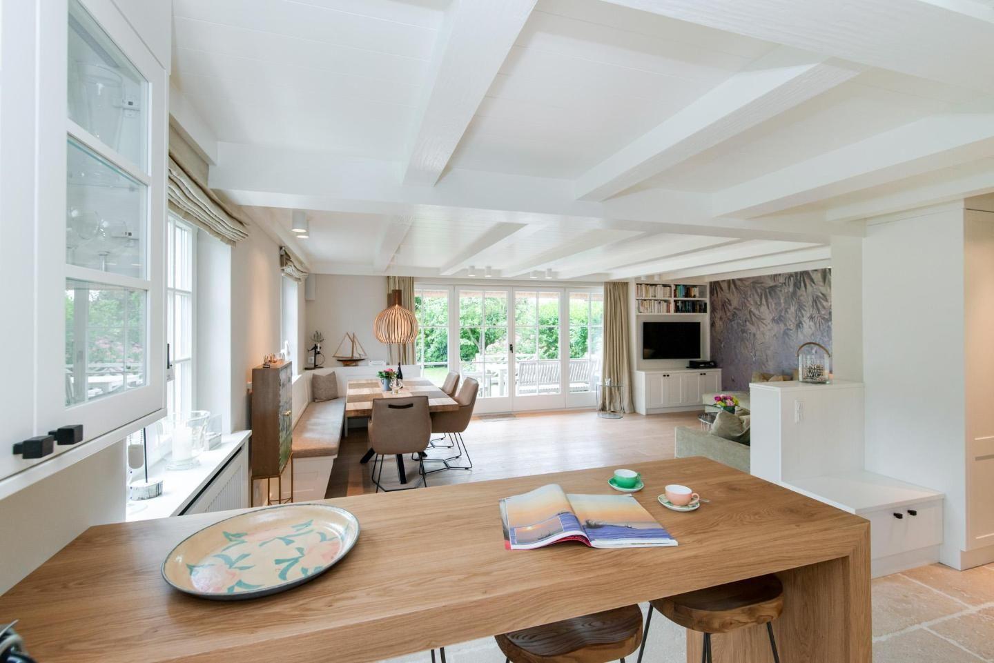 Bright kitchen with dining area and living room with TV and balcony door.