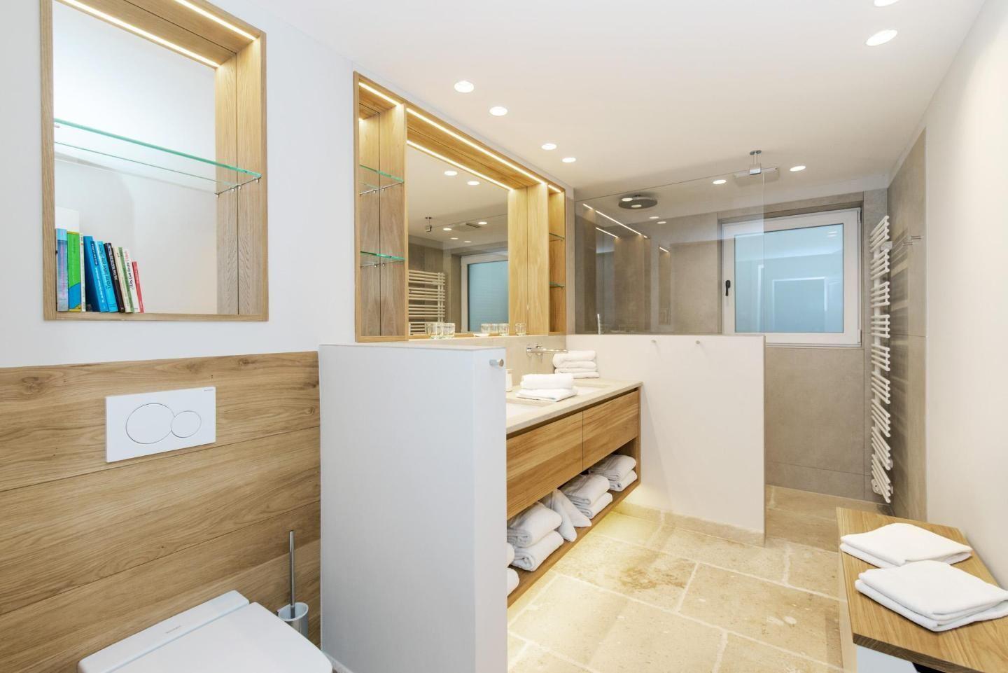 Modern bathroom with wooden shelves and mirrors. White tiles and towels.