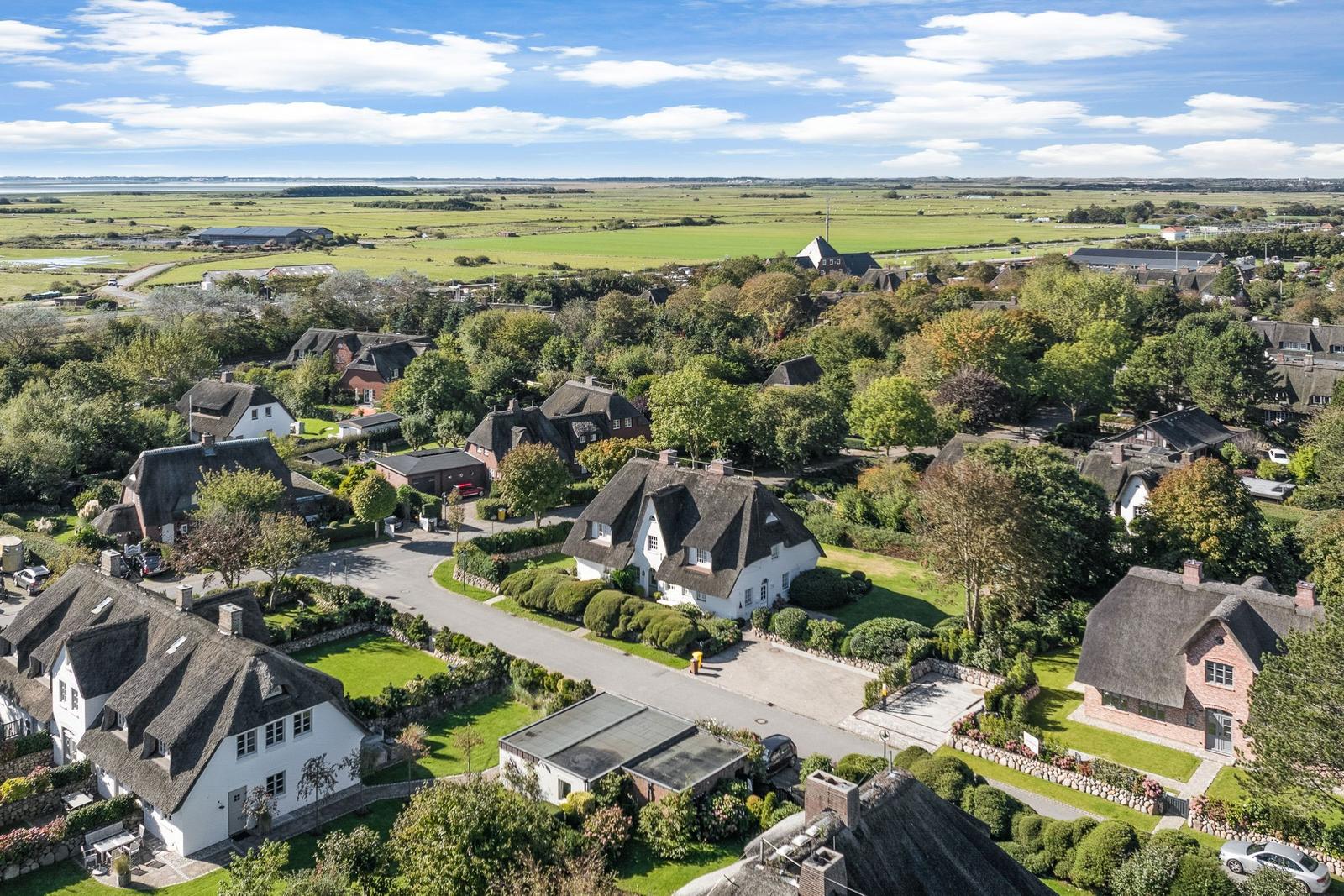 Dorf mit strohgedeckten Häusern und grünen Wiesen unter blauem Himmel.