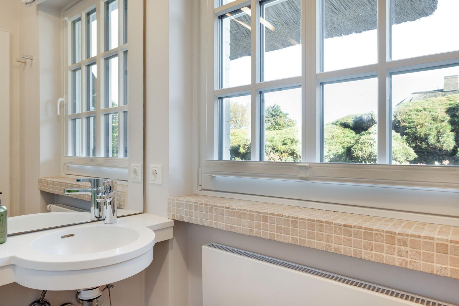Badezimmer mit Waschbecken, Spiegel und Fensterblick auf Grünflächen.
