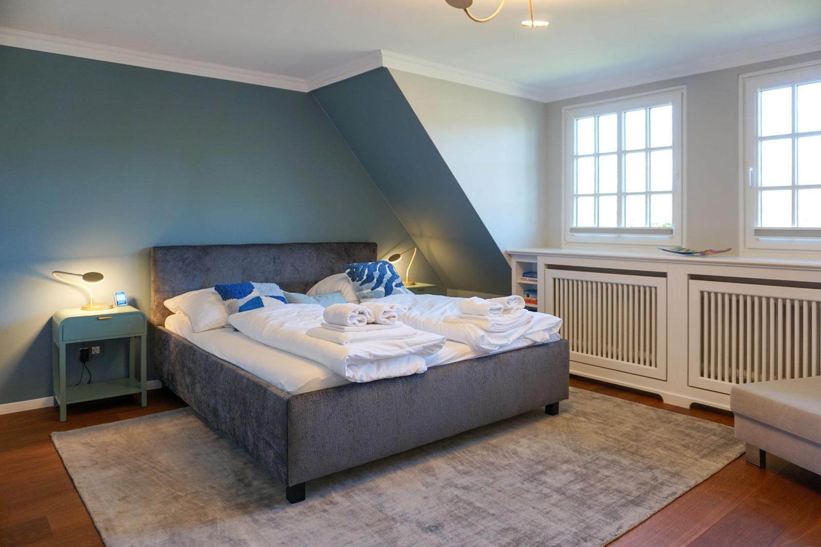 Schlafzimmer mit Bett, Nachttisch und Fenstern