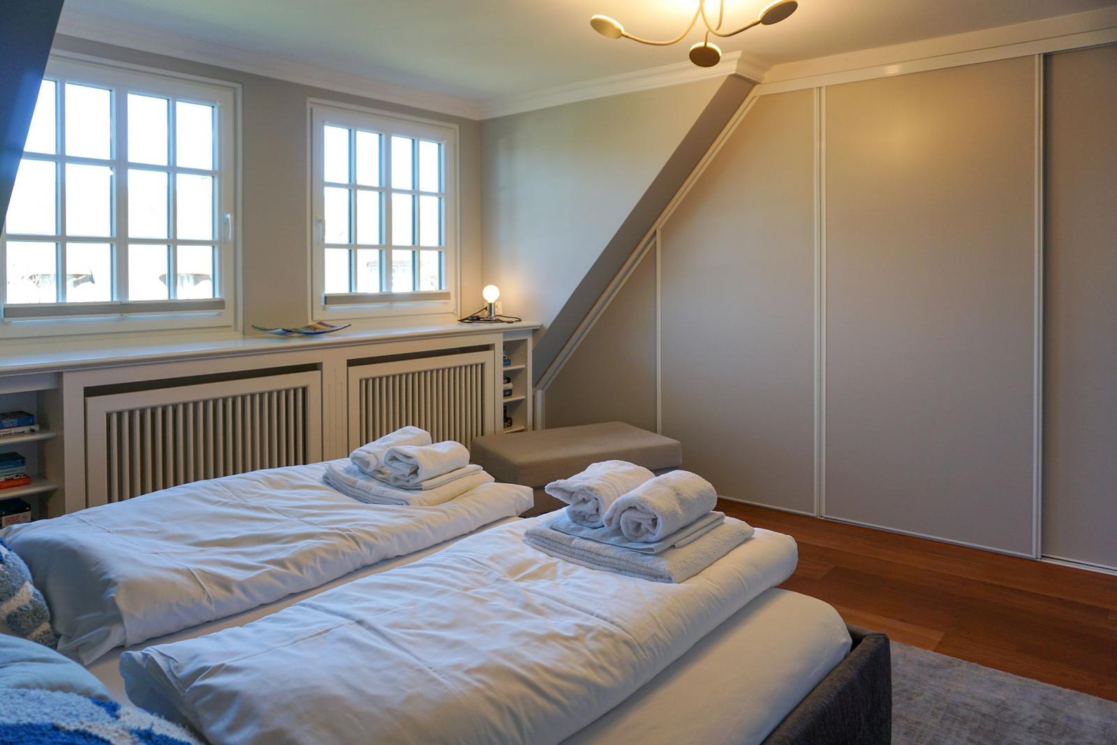 Zwei Betten mit weißen Bettwäsche und Handtüchern. Fenster, Schrank und Holzboden.