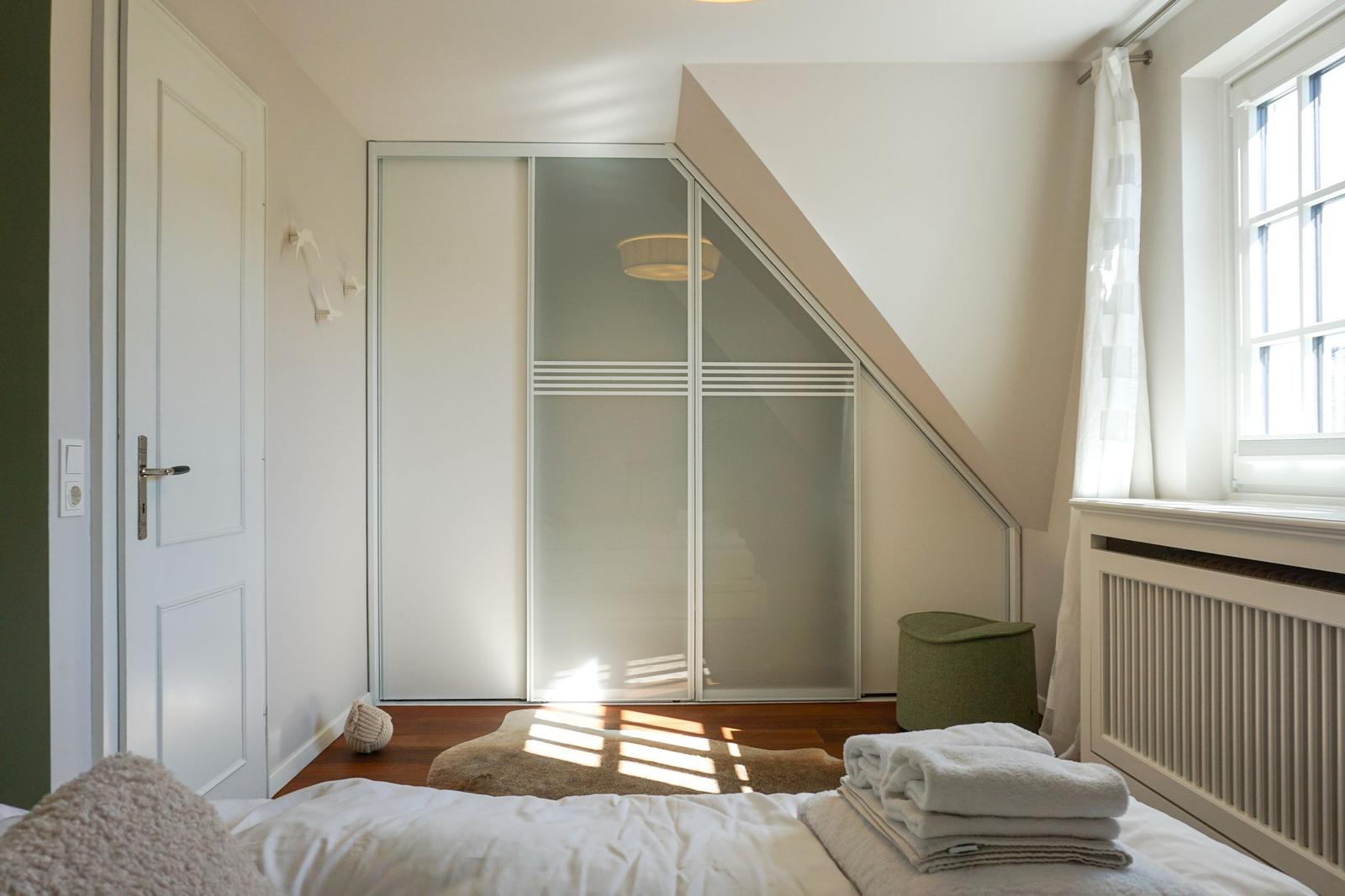 Schlafzimmer mit Dachschrägen, Kleiderschrank und Fenster.