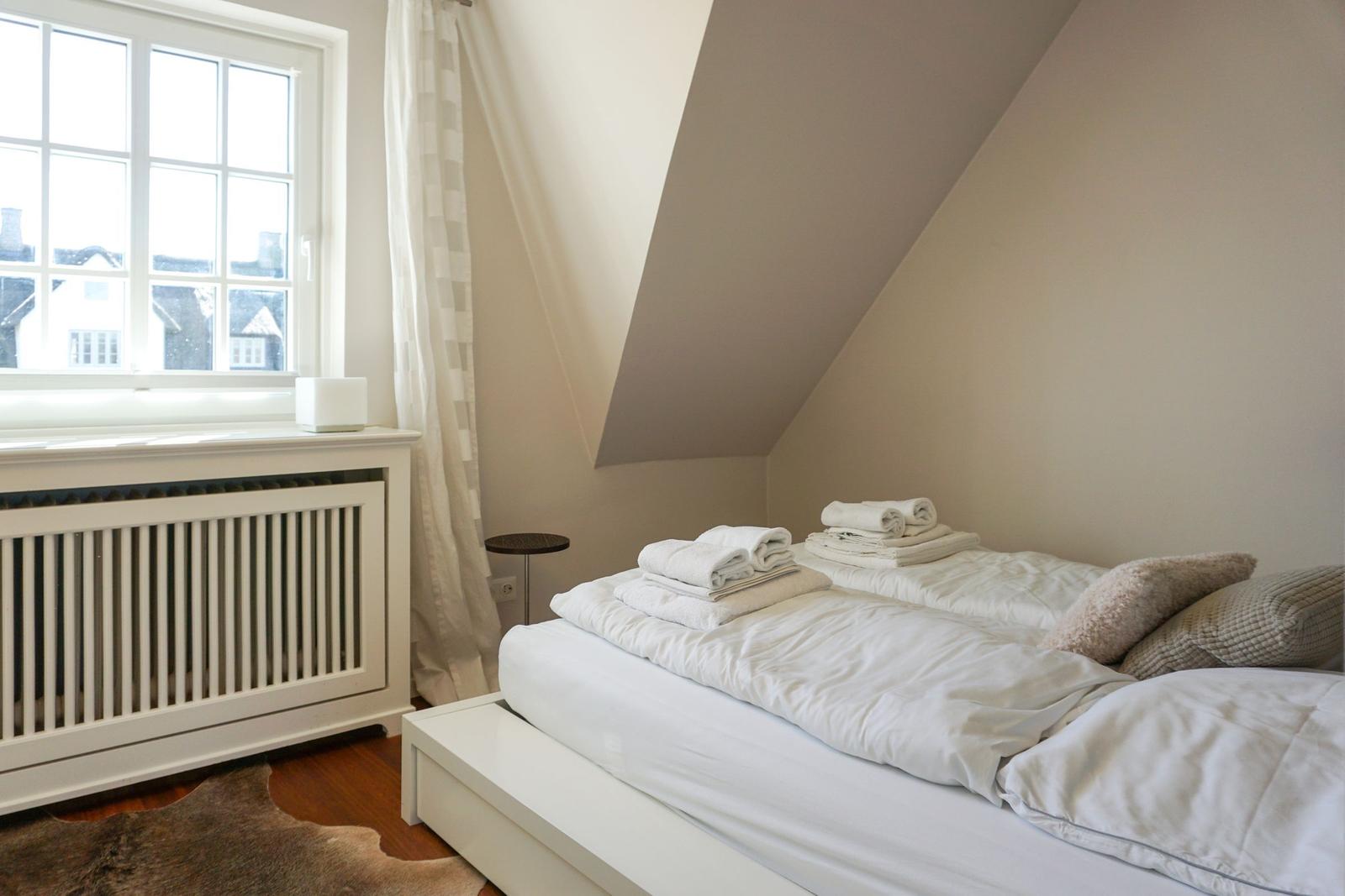 Schlafzimmer mit Dachschräge, Fenster und Bett mit Handtüchern.