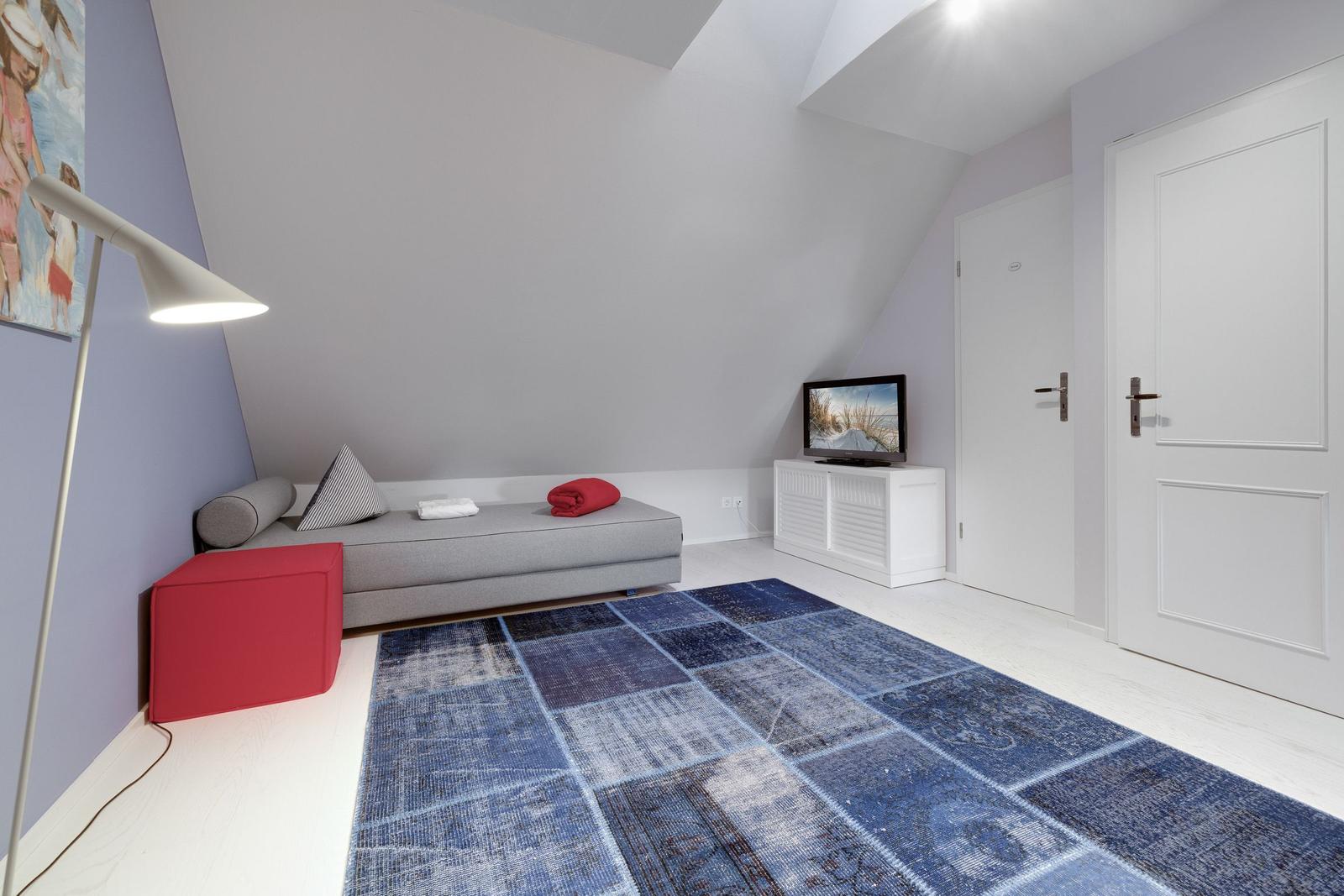 Schlafzimmer mit Dachschräge, Sofa, Teppich und Fernseher.
