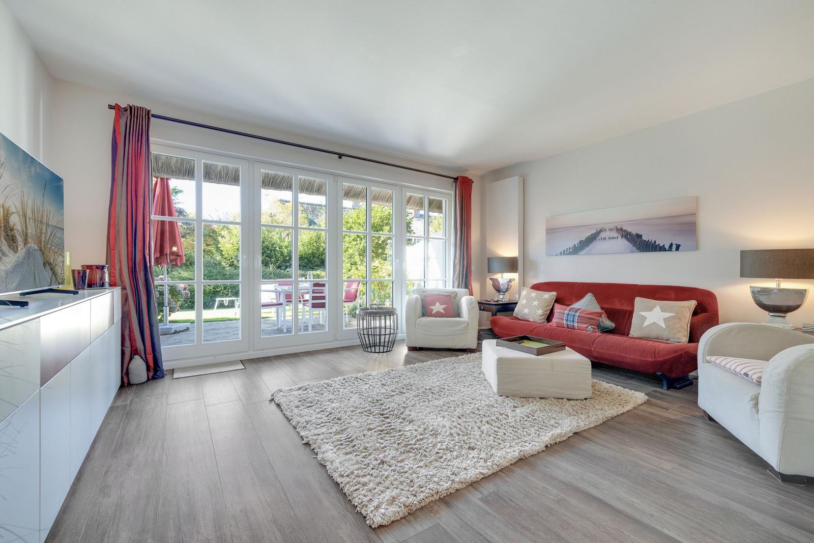 Wohnzimmer mit rotem Sofa, weißen Sesseln und Blick auf den Garten.
