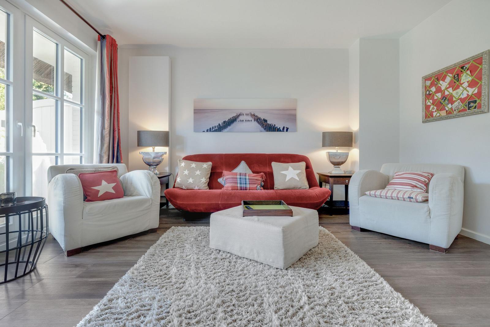 Ein Wohnzimmer mit rotem Sofa, zwei weißen Sesseln und einem flauschigen Teppich.