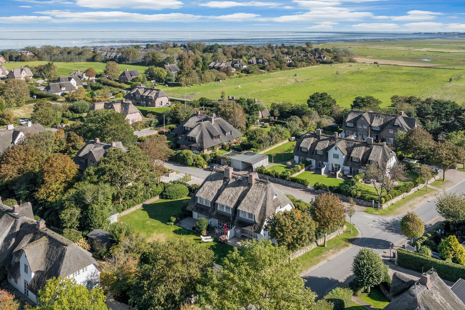 Dorf mit strohgedeckten Häusern und grünen Wiesen am Wasser.