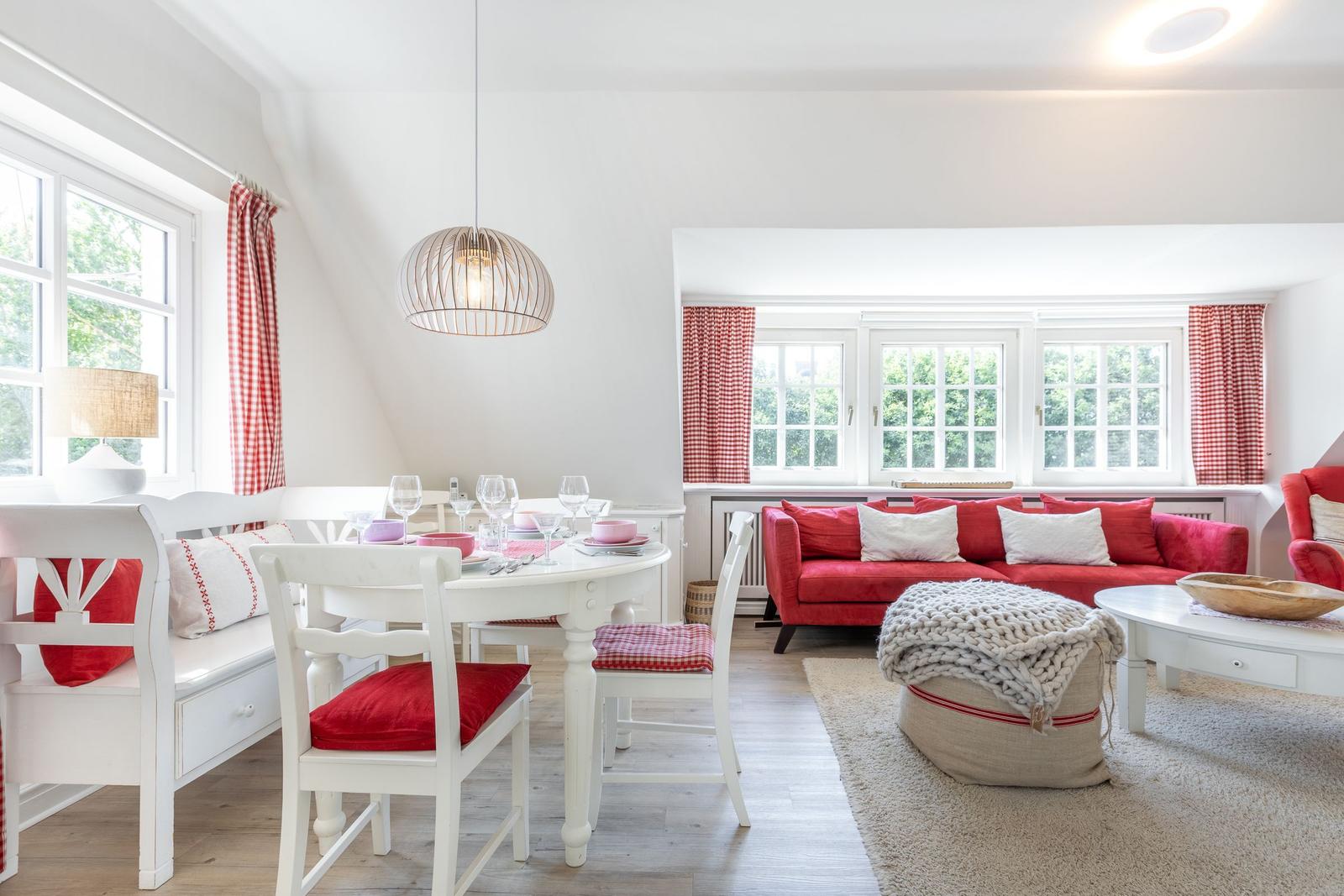 Wohn- und Essbereich mit rotem Sofa, weißem Tisch und Stühlen sowie roten Gardinen.