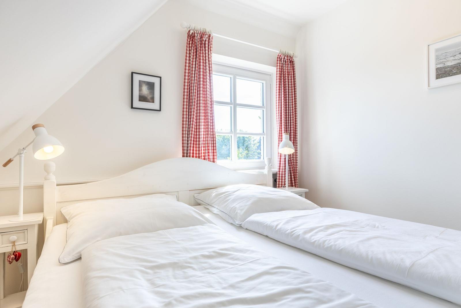 Zimmer mit Doppelbett, Fenster und roten Gardinen.