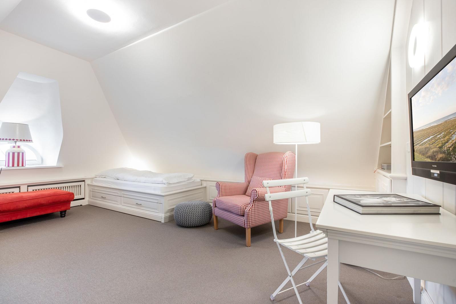 Schlafzimmer mit Bett, Sessel, Schreibtisch und TV.