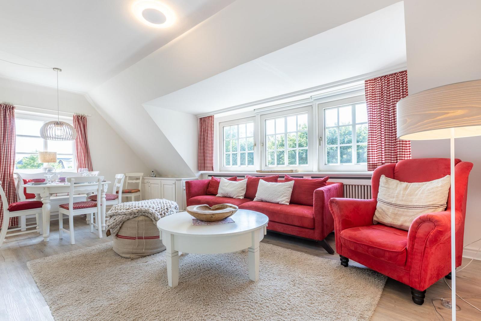 Wohn- und Essbereich mit rotem Sofa, Stuhl und Gardinen.