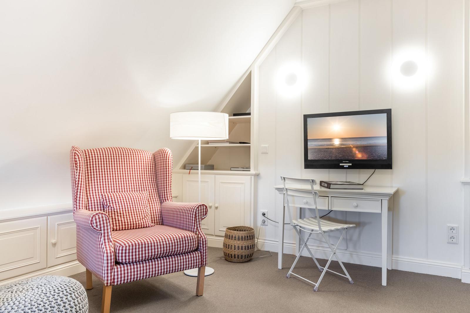 Ein Raum mit Sessel, Schreibtisch und Fernseher an der Wand.