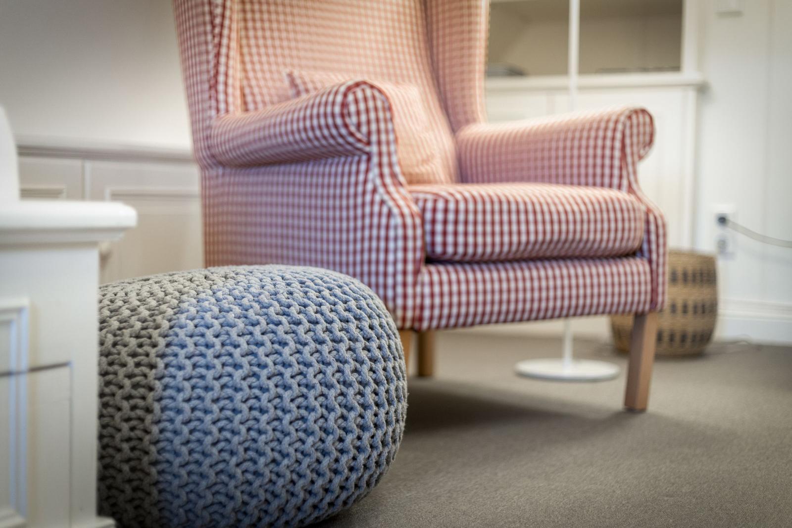Ein Sessel mit kariertem Stoff und ein gestrickter Hocker stehen im Raum.