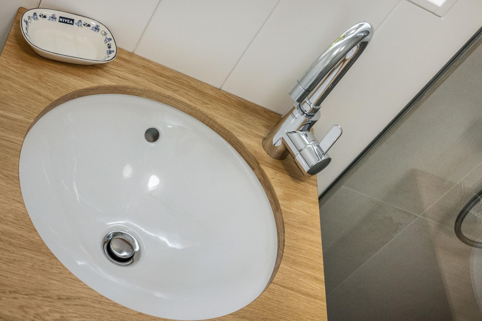 Waschbecken mit Wasserhahn auf Holzplatte, daneben Seifenschale.