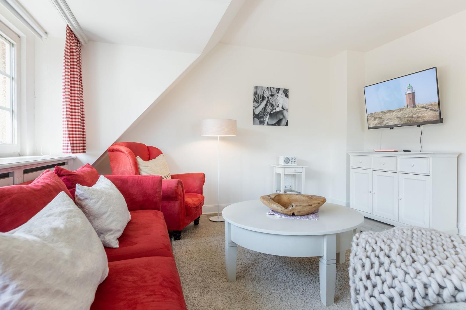 Wohnzimmer mit rotem Sofa, weißem Tisch und Fernseher an der Wand.