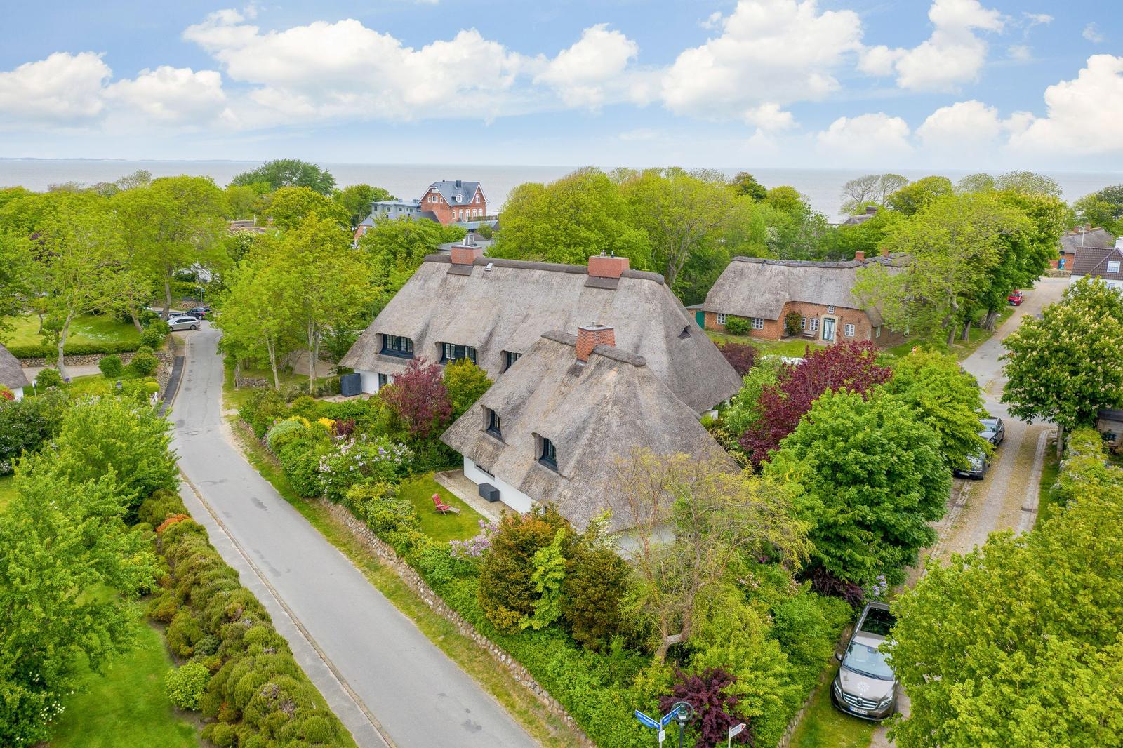 Thatched-roof house surrounded by trees and garden. View of the sea.