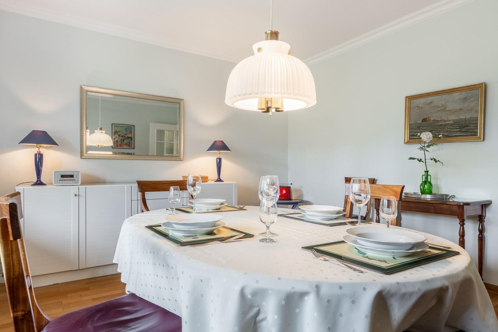 Round table set for six, illuminated by a ceiling lamp.