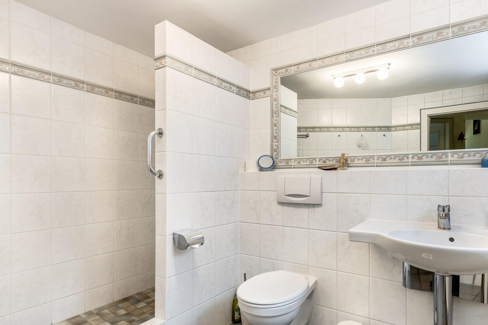 Bathroom with shower, toilet, and sink. Tiled wall with decorative border.