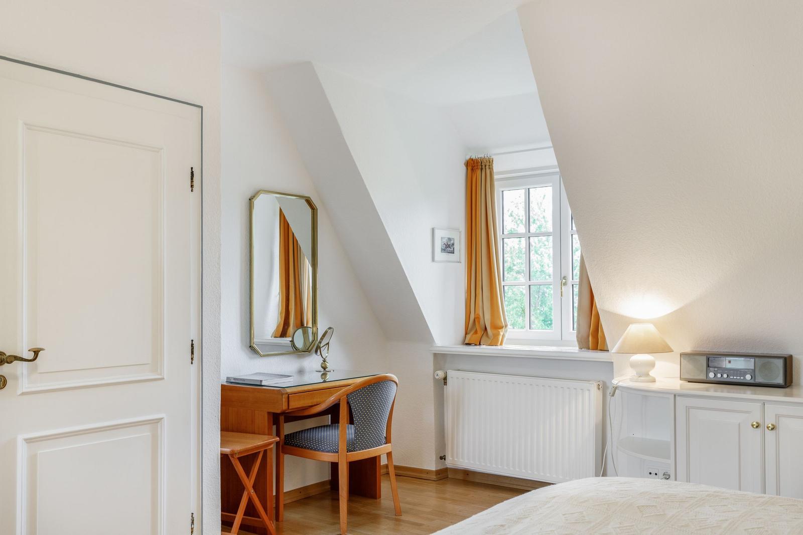 Bedroom with desk, mirror, and window with curtains.