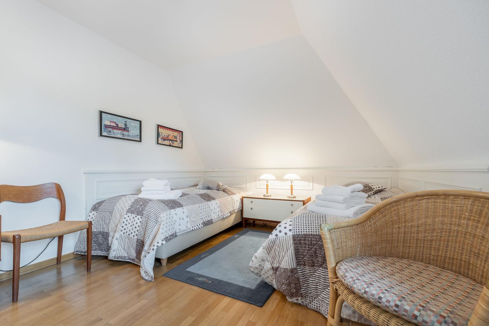 Two beds with patterned bedspreads, wooden floor, and desk in attic room.