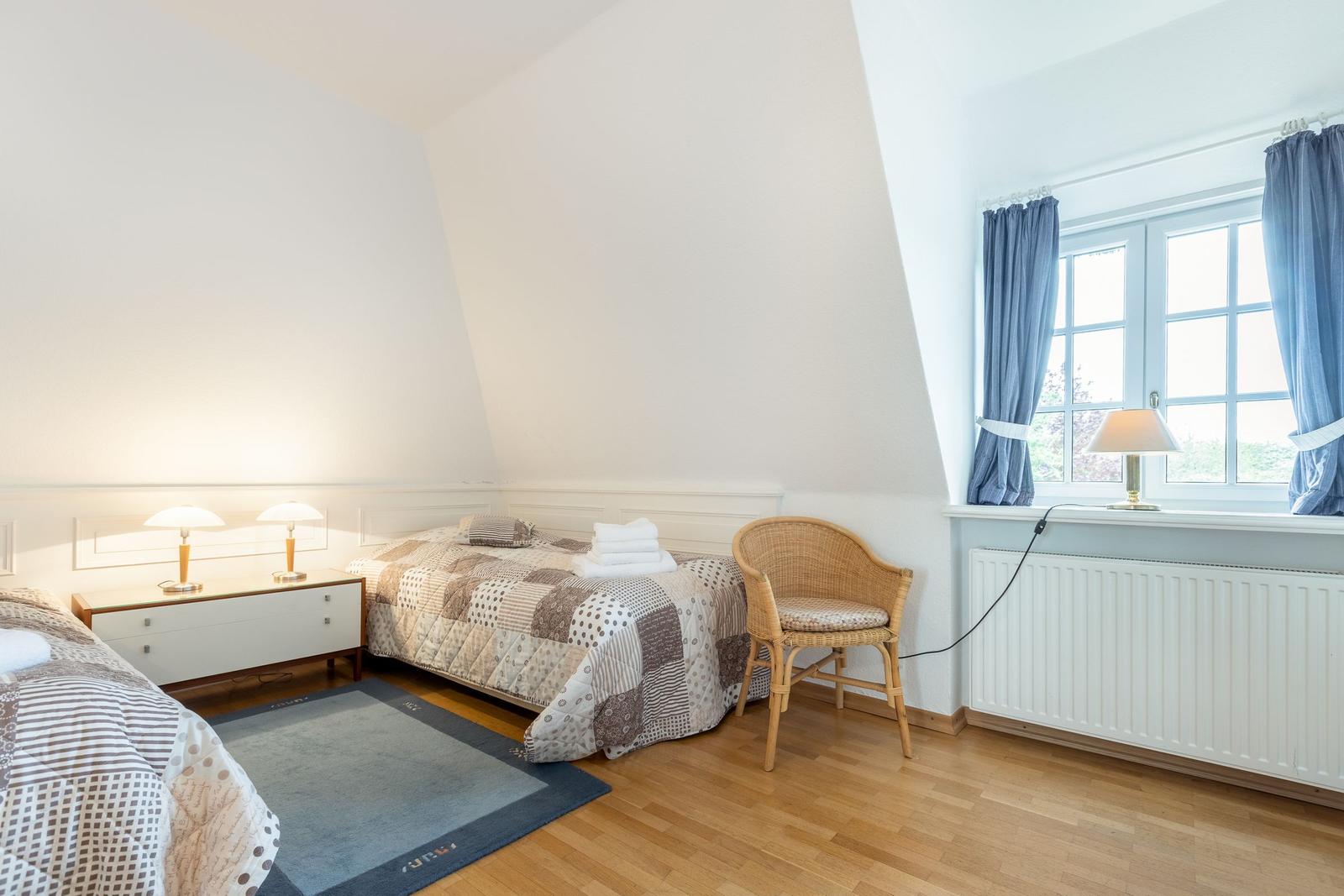 Bedroom with sloped ceiling, bed, nightstand, chair, and window.