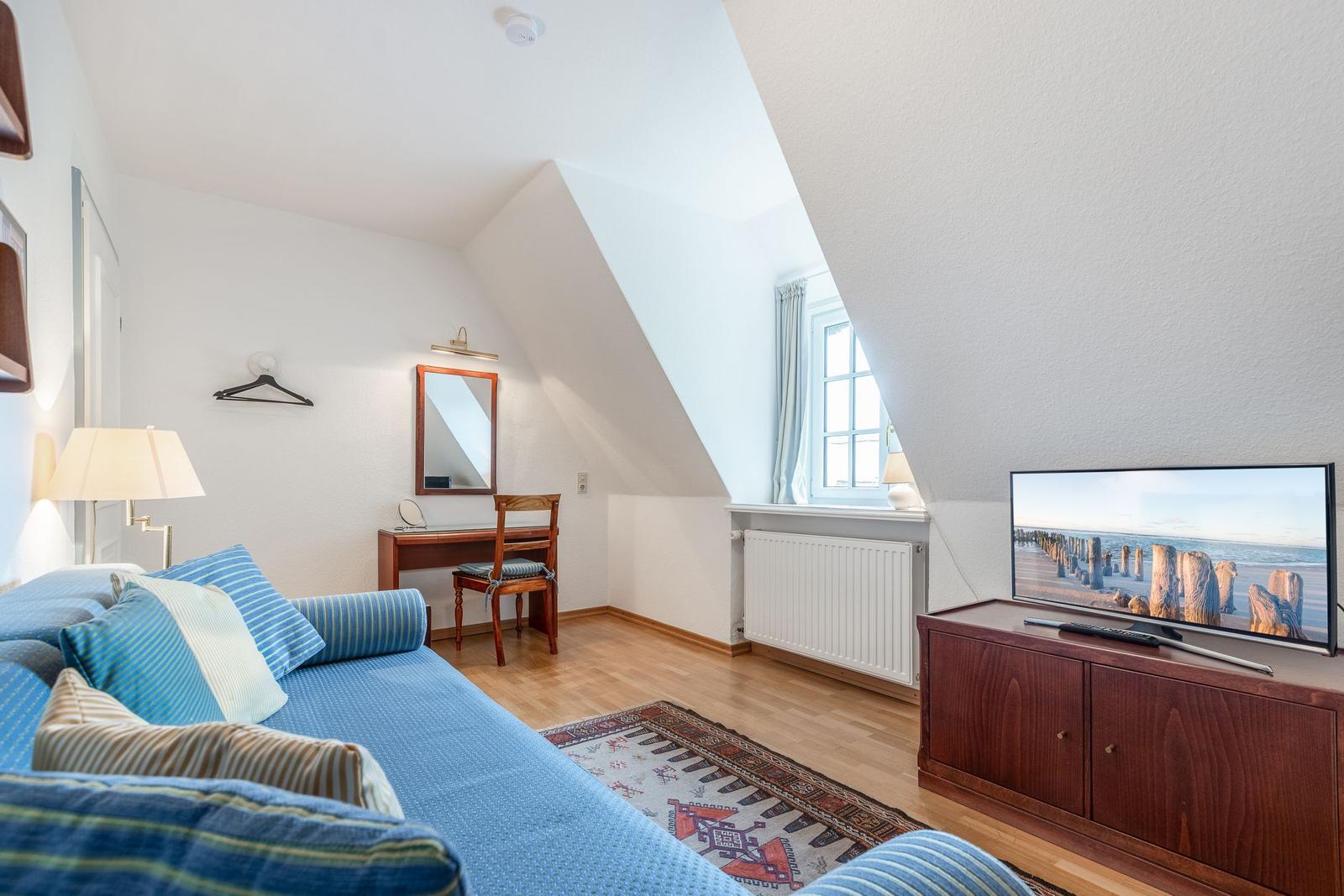 A bedroom with sloped ceiling, sofa, desk, and TV.