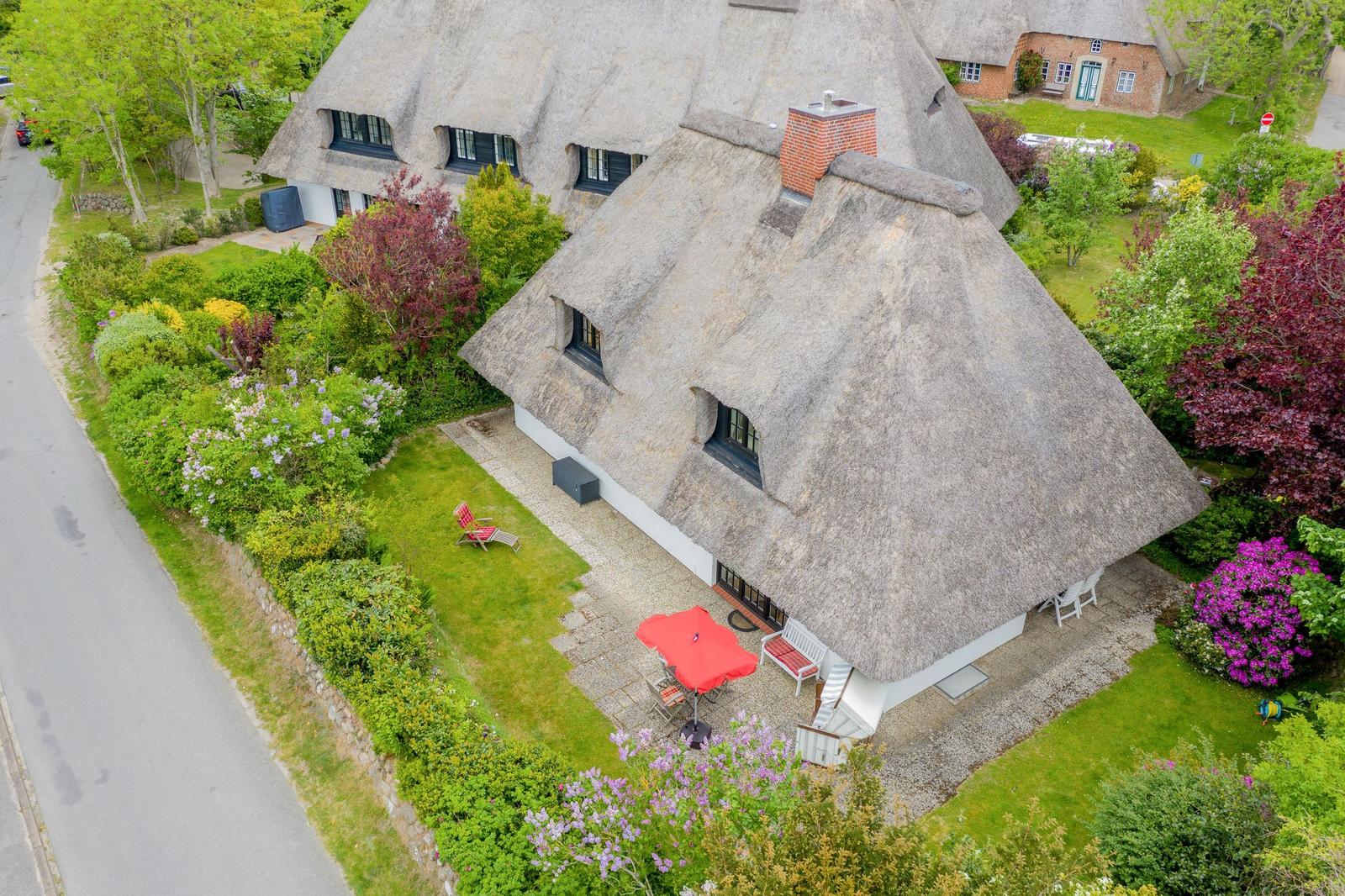 Thatched house with garden and terrace with red umbrella.
