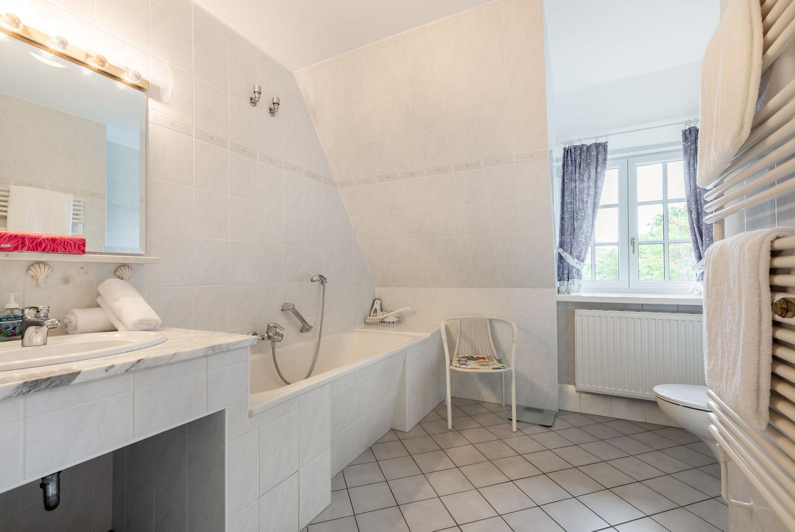 Bathroom with bathtub, sink, and toilet. Window with curtains and radiator.