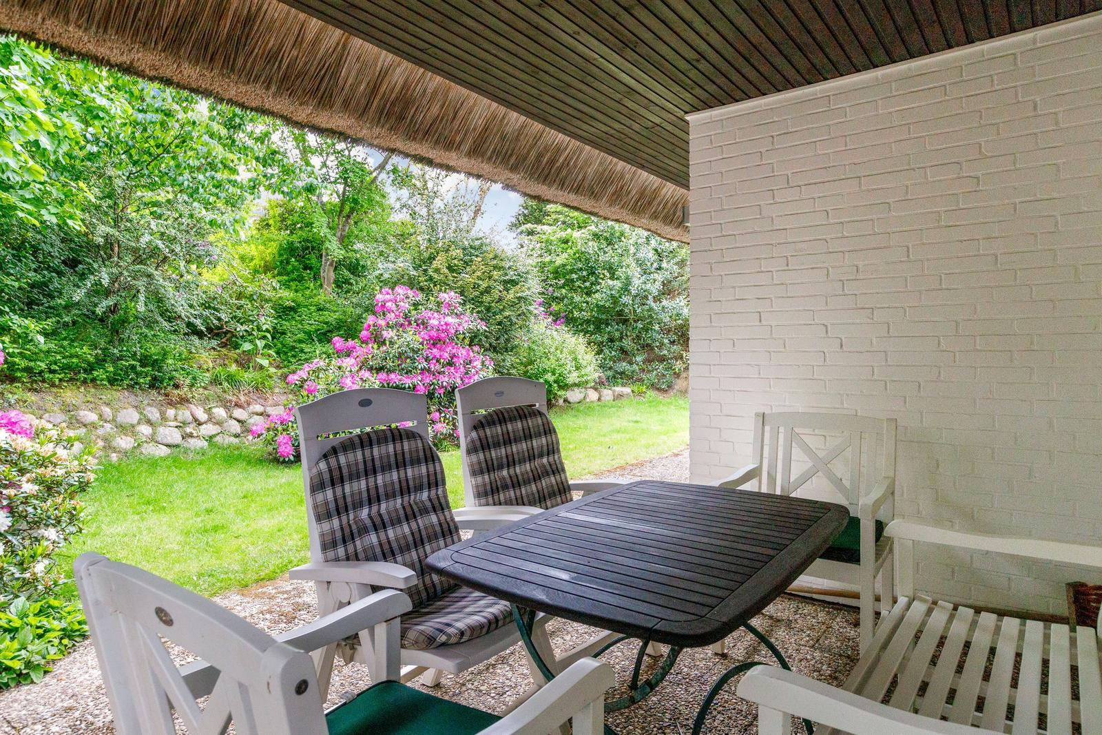 Patio with table and chairs, view of green garden with pink flowers.