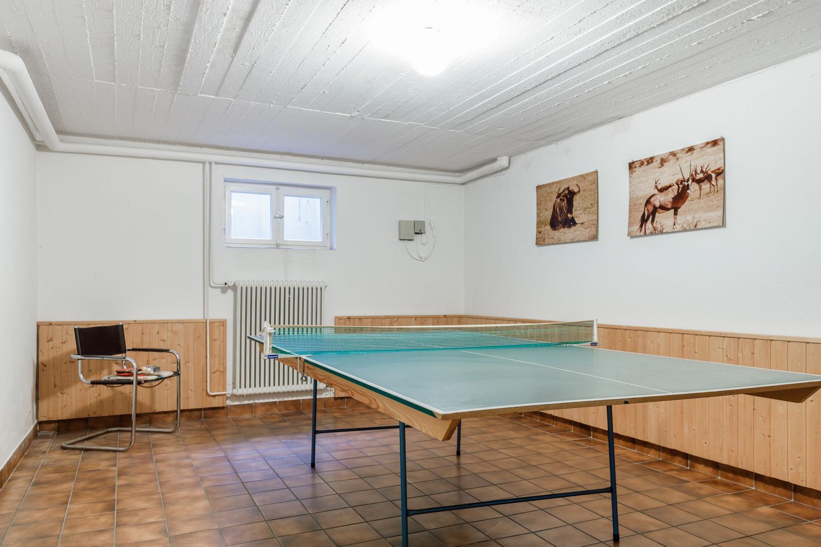 Ping pong table with net, wall pictures and window in room.