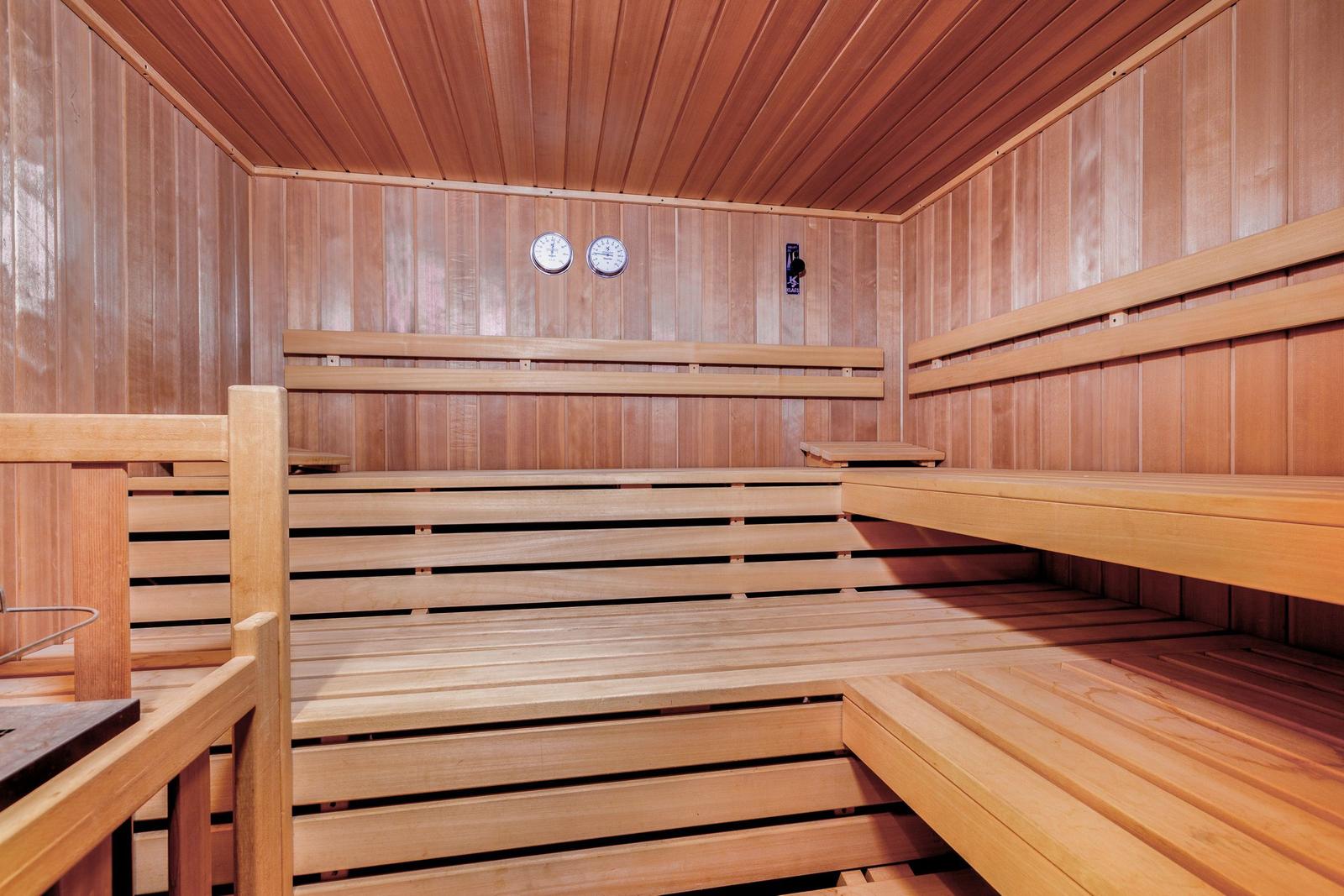 Wooden sauna with multiple benches and two thermometers on the wall.