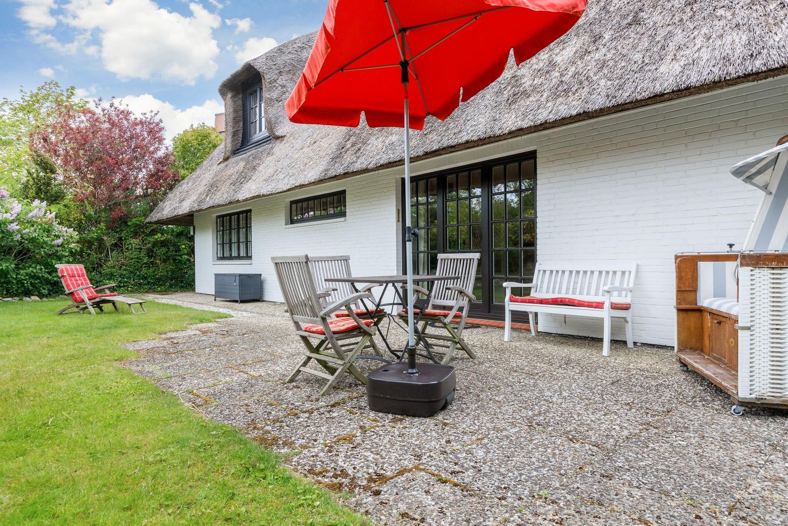 House with thatched roof and garden area with table, chairs, and umbrella.