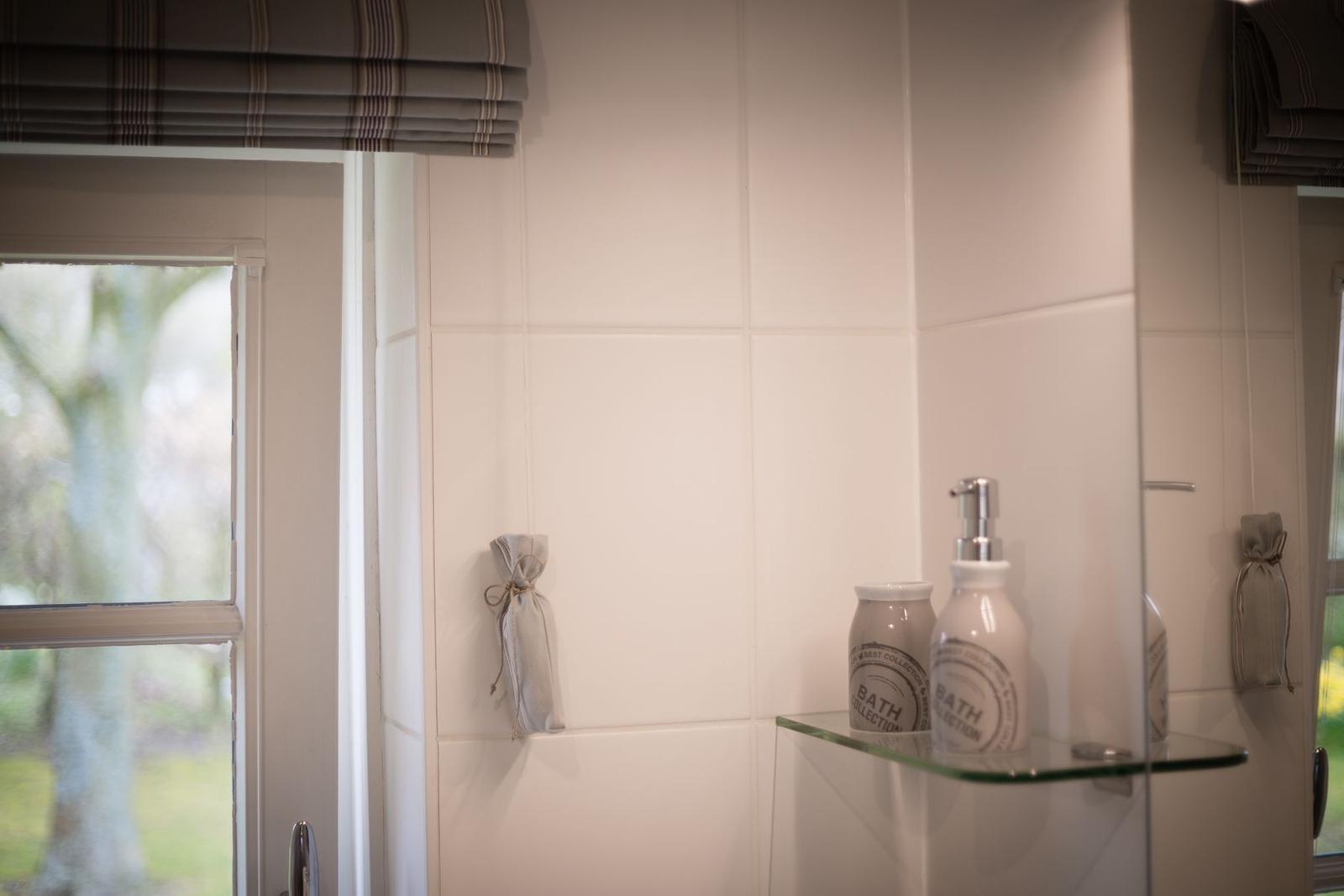 Bathroom with window, white tiles, and glass shelf with care products.