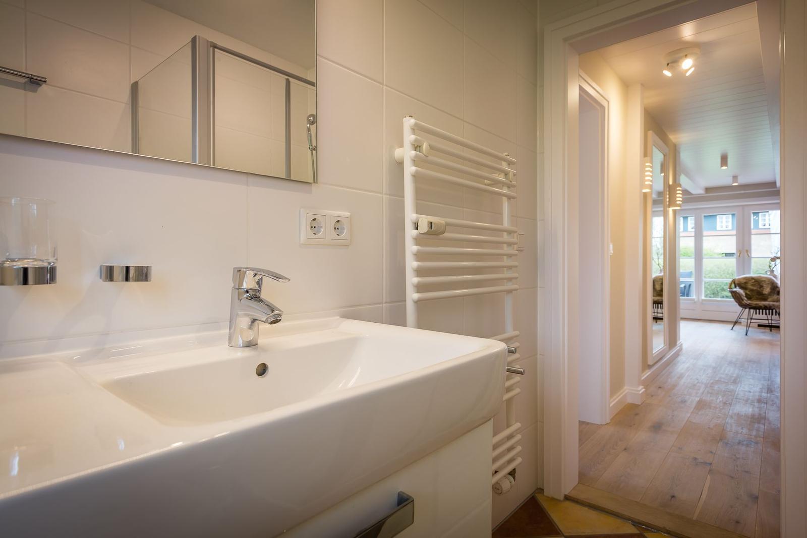 Bathroom with sink, mirror, and heater. Hallway to living area with wooden floor.
