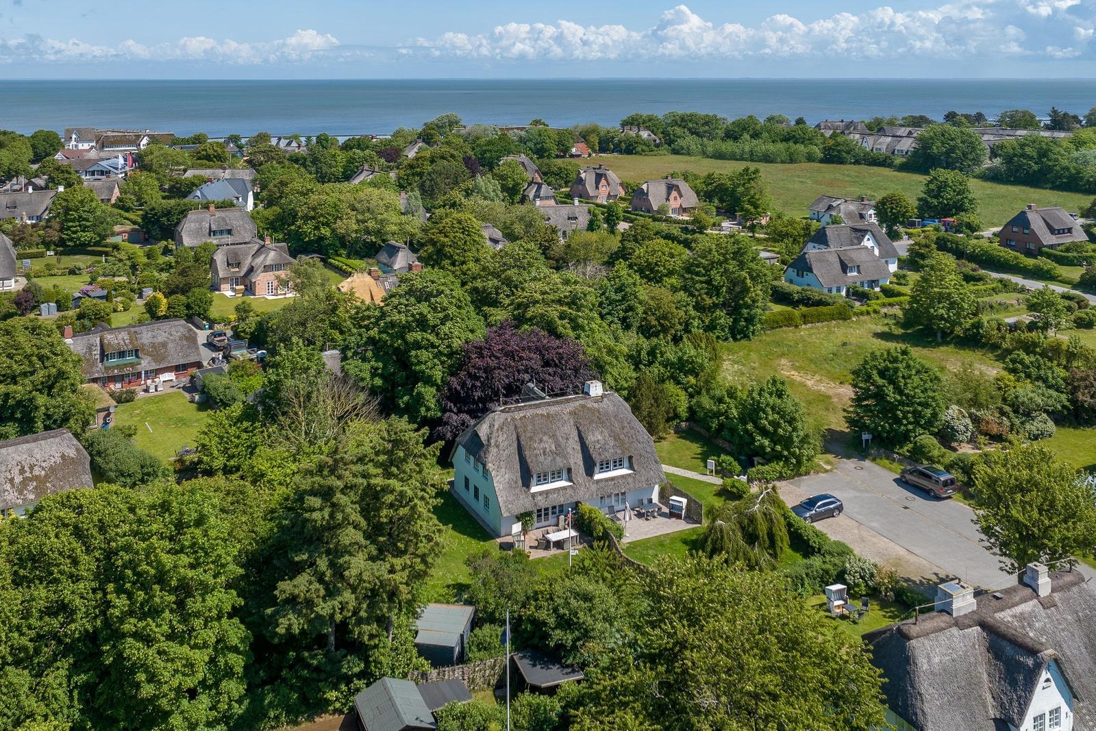 House with thatched roof, surrounded by greenery and trees, view of sea and sky.