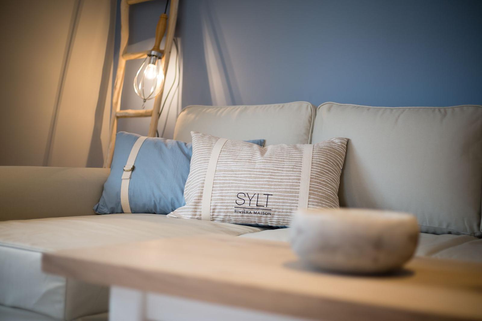 Sofa with cushions and wooden table. Background: wall and lamp.