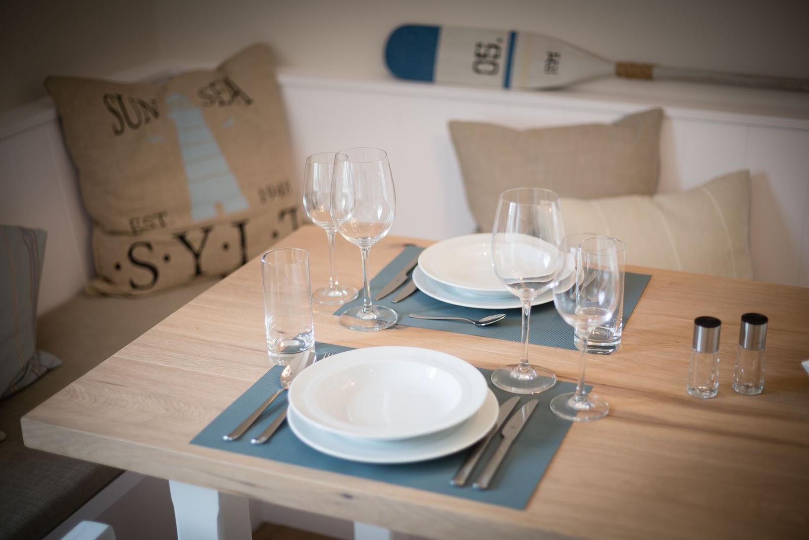 Dining table set for two with kitchen seating in the background.
