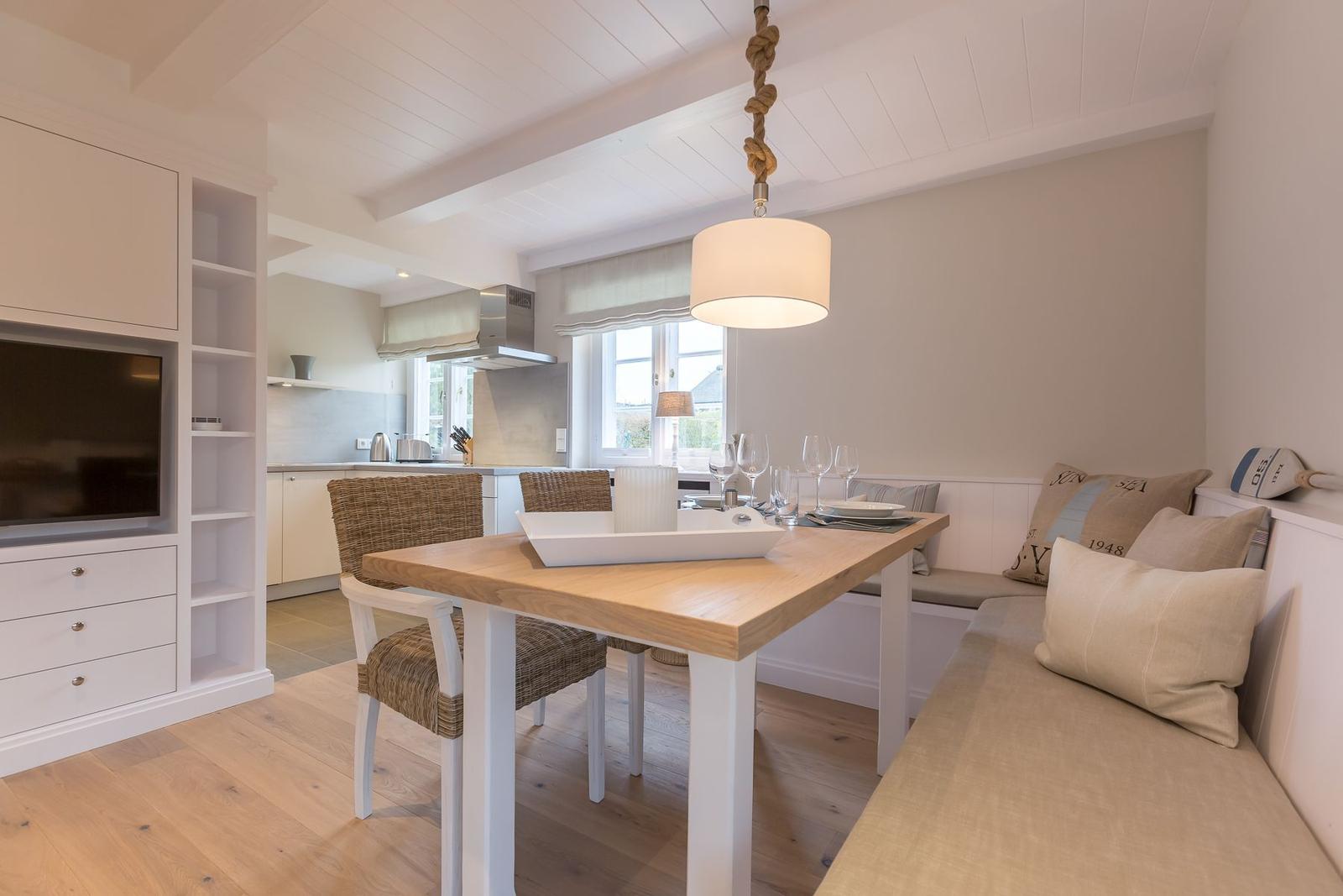 Dining area with wooden table, bench seating, and kitchen area in background.