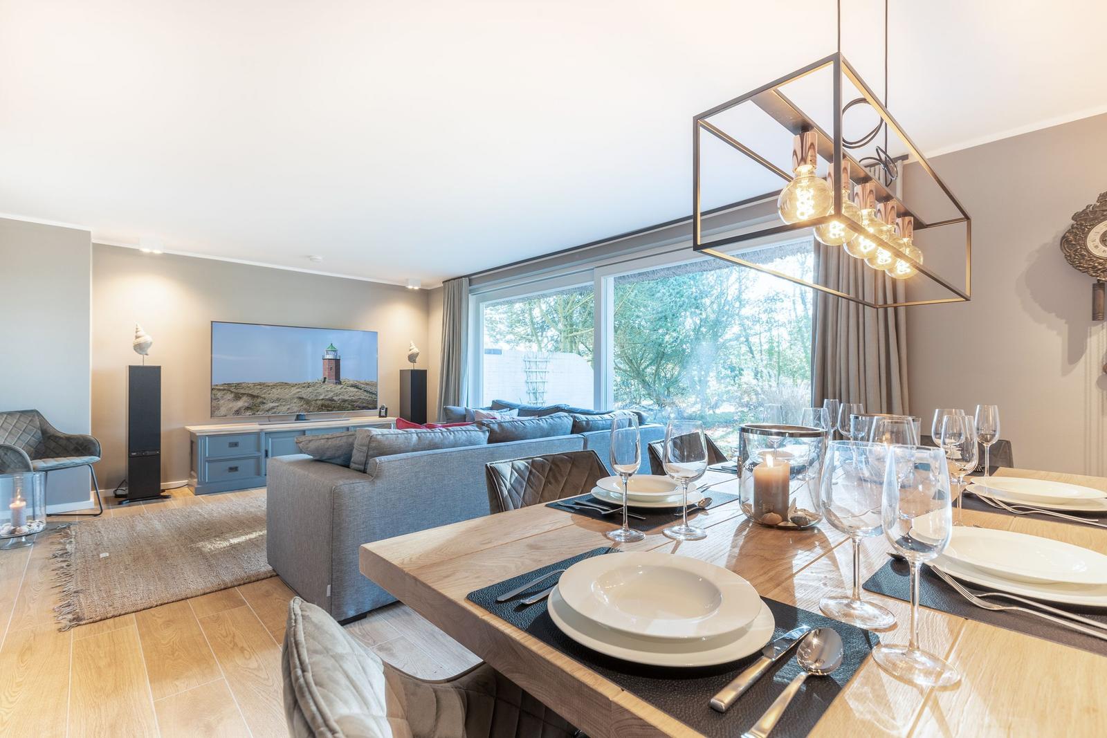 Esszimmer mit Holztisch und moderner Beleuchtung. Wohnbereich mit Sofa und Fernseher.