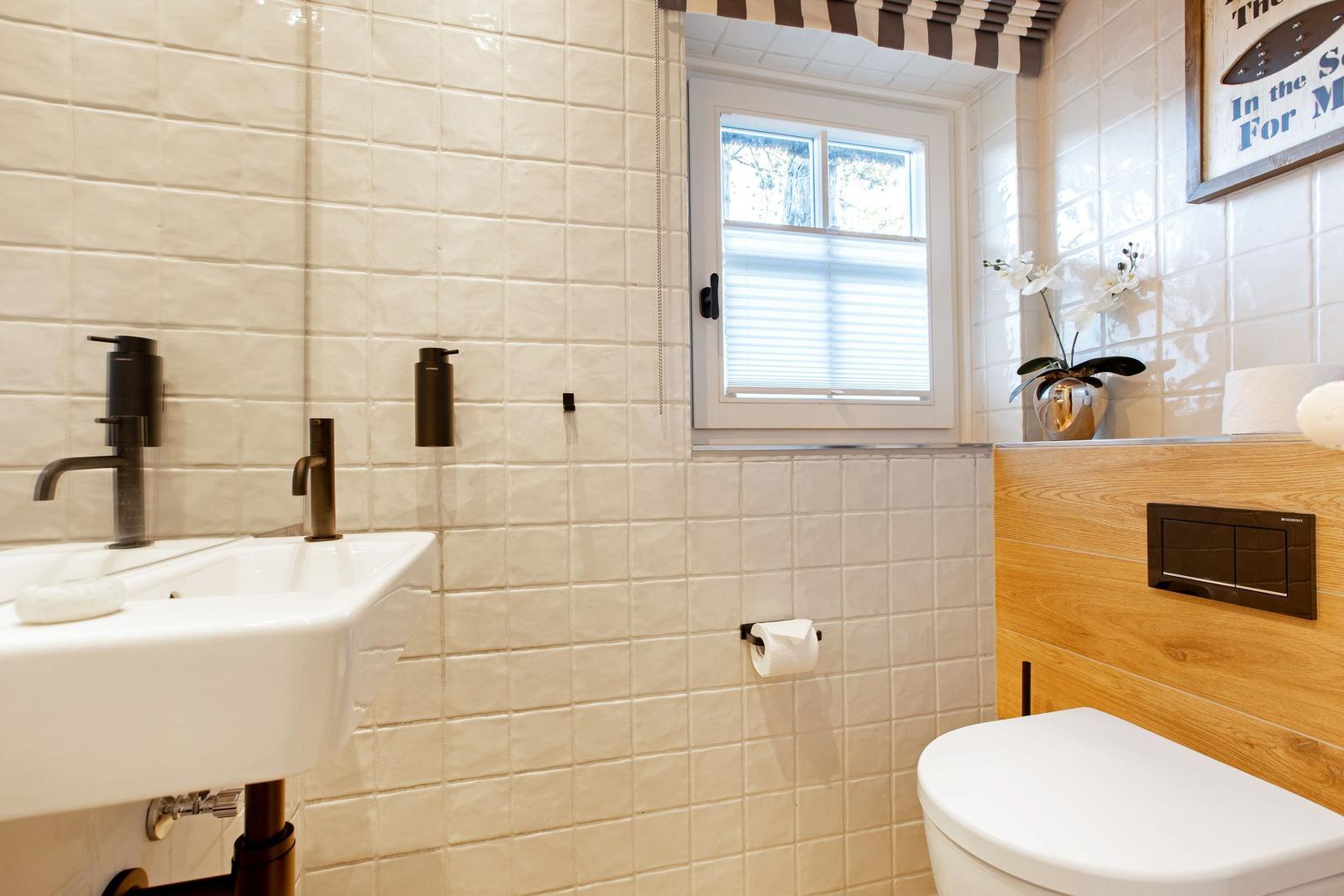 Badezimmer mit Waschbecken, Toilette und Fenster mit Jalousie.